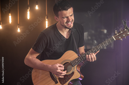 Happy guitarist in a black t-shirt plays an acoustic guitar at a concert against a blurred black background. Close up.