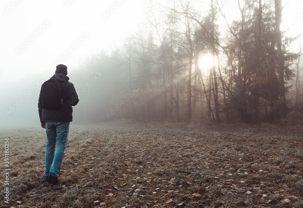 Young man walking on meadow with autumn forest in freeze misty morning fog and sun. Czech landscape Young man walking on meadow with autumn forest in freeze misty morning fog and sun. Czech landscape