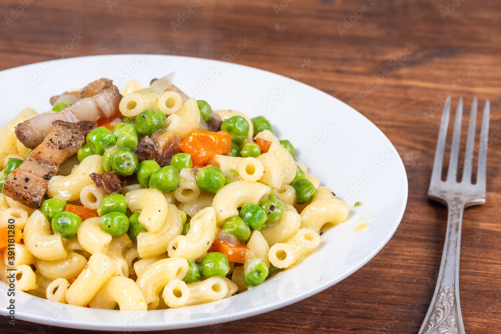 Traditional italian chifferini pasta with peas, carrots and toasted pancetta on a plate on a rustic wooden table, background Traditional italian chifferini pasta with peas, carrots and toasted pancetta on a plate on a rustic wooden table, background