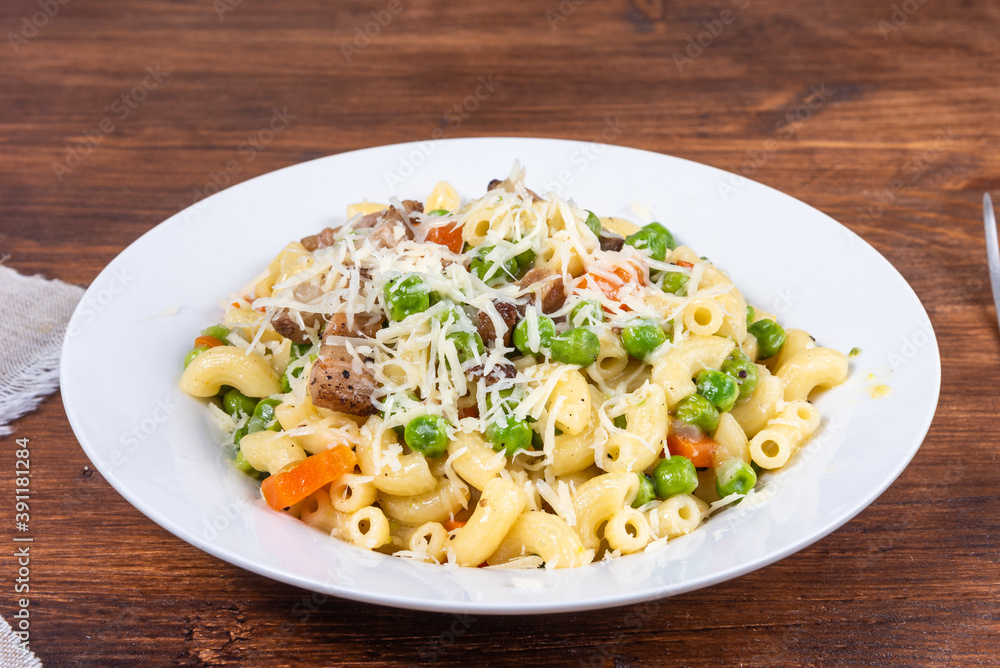 Traditional italian chifferini pasta with peas, carrots and toasted pancetta, sprinkled with grated cheese on a plate on a rustic wooden table, background Traditional italian chifferini pasta with peas, carrots and toasted pancetta, sprinkled with grated cheese on a plate on a rustic wooden table, background