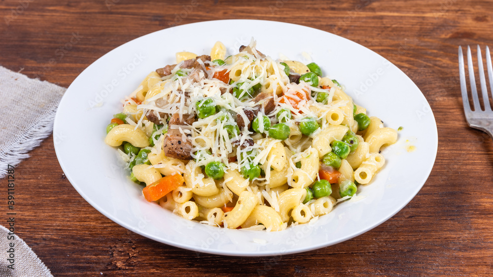 Traditional italian chifferini pasta with peas, carrots and toasted pancetta, sprinkled with grated cheese on a plate on a rustic wooden table, background Traditional italian chifferini pasta with peas, carrots and toasted pancetta, sprinkled with grated cheese on a plate on a rustic wooden table, background