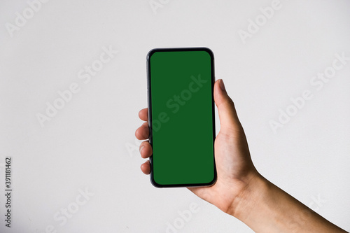 Hand holding white mobile phone with blank mint green screen in white background.