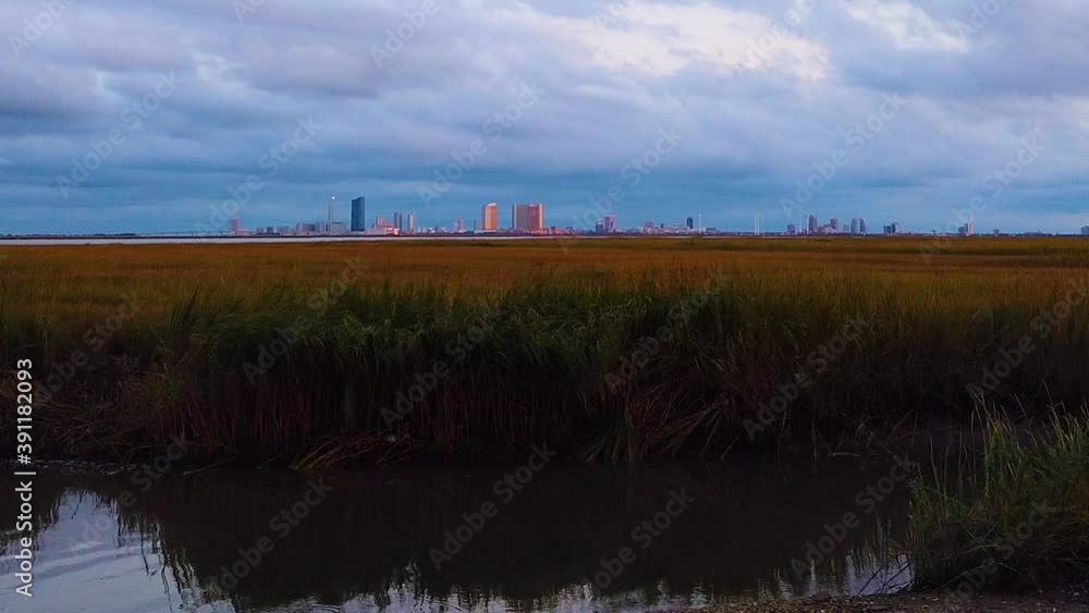 HD MOTIONLAPSE Straight tilt up Atlantic City skyline in distance over waterway with mostly cloudy sky day to night with clouds turning pink, purple and blue HD MOTIONLAPSE Straight tilt up Atlantic City skyline in distance over waterway with mostly cloudy sky day to night with clouds turning pink, purple and blue