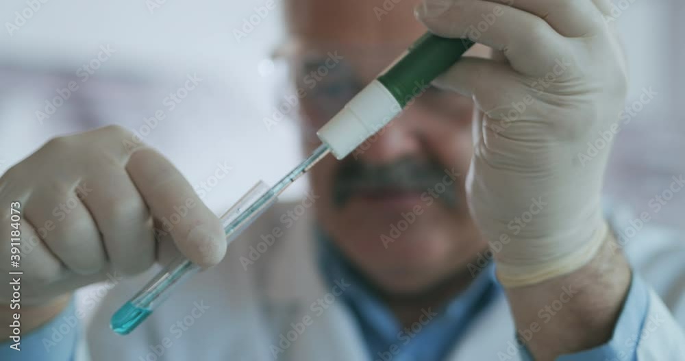 Technician carefully drips the solution from the pipette into glass tubes for DNA analysis. Doctor Drips Blue Solution Into Glass Tube, Coronavirus Pandemic, Hands Closeup. Technician carefully drips the solution from the pipette into glass tubes for DNA analysis. Doctor Drips Blue Solution Into Glass Tube, Coronavirus Pandemic, Hands Closeup.