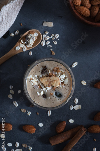 Tasty smoothie with banana and oatmeal, muesli and almond milk in a glass. On a dark gray concrete stone background, with ingredients for cooking. Bio. Top view.
