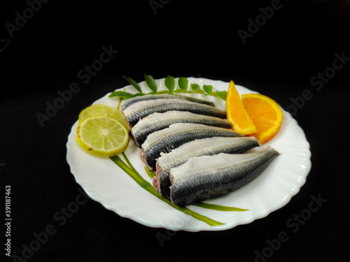 Cleaned and ready to cook fresh indian sardine decorated with curry leaves,lemon slice and tomato slice .Isolated on black background. photo