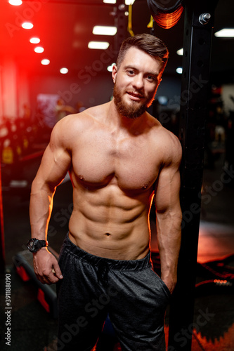 Bodybuilder is posing. Beautiful sporty guy male power. Fitness muscled man without shirt on dark gym background.