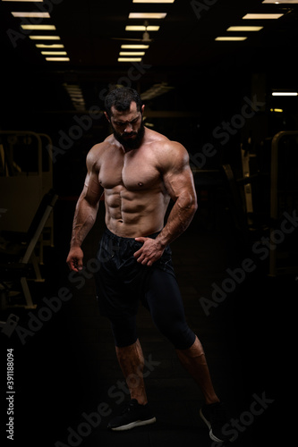 strong young athlete bearded male with perfect athletic physique body in dark hight sport gym posing like super hero