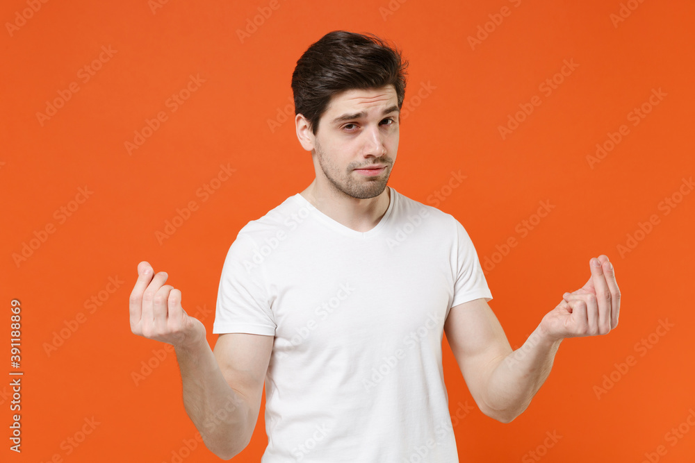 Handsome young man 20s wearing basic casual white empty blank t-shirt standing rubbing fingers showing cash gesture asking for money isolated on bright orange colour wall background, studio portrait. Handsome young man 20s wearing basic casual white empty blank t-shirt standing rubbing fingers showing cash gesture asking for money isolated on bright orange colour wall background, studio portrait.