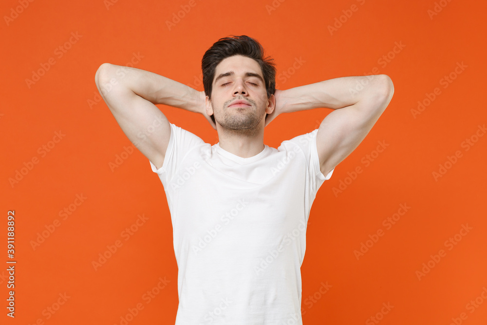 Relaxed tired young man 20s wearing basic casual white blank empty t-shirt standing sleep with hands behind head keeping eyes closed isolated on bright orange colour wall background, studio portrait. Relaxed tired young man 20s wearing basic casual white blank empty t-shirt standing sleep with hands behind head keeping eyes closed isolated on bright orange colour wall background, studio portrait.