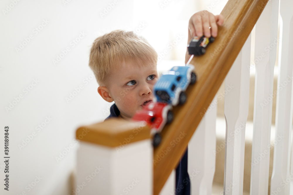 A three year old boy playing with his toy cars on the stair bannister. A three year old boy playing with his toy cars on the stair bannister.