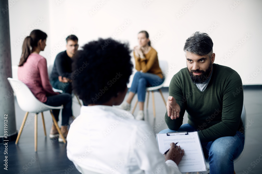 Mid adult man talking to female psychotherapist during group therapy.