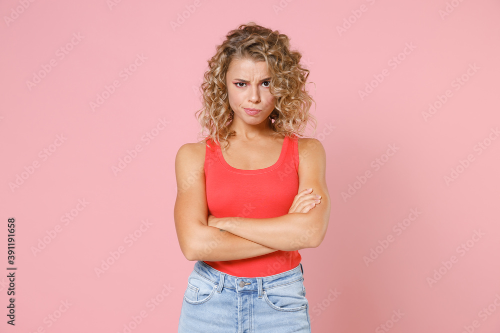 Confused dissatisfied displeased puzzled young blonde woman wearing basic casual tank top standing holding hands crossed looking camera isolated on pastel pink colour wall background, studio portrait. Confused dissatisfied displeased puzzled young blonde woman wearing basic casual tank top standing holding hands crossed looking camera isolated on pastel pink colour wall background, studio portrait.