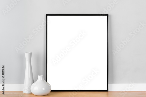 Elegant vertical black picture frame poster artwork mockup template for online shop with white vases in front of  light grey wall. Blank image area masked with clipping path.