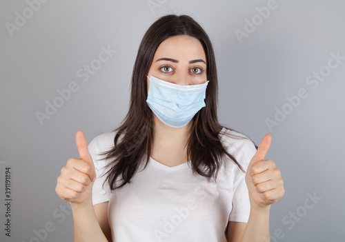 Portrait of young woman wearing medical mask at gray background. Coronavirus concept. © ANAHIT