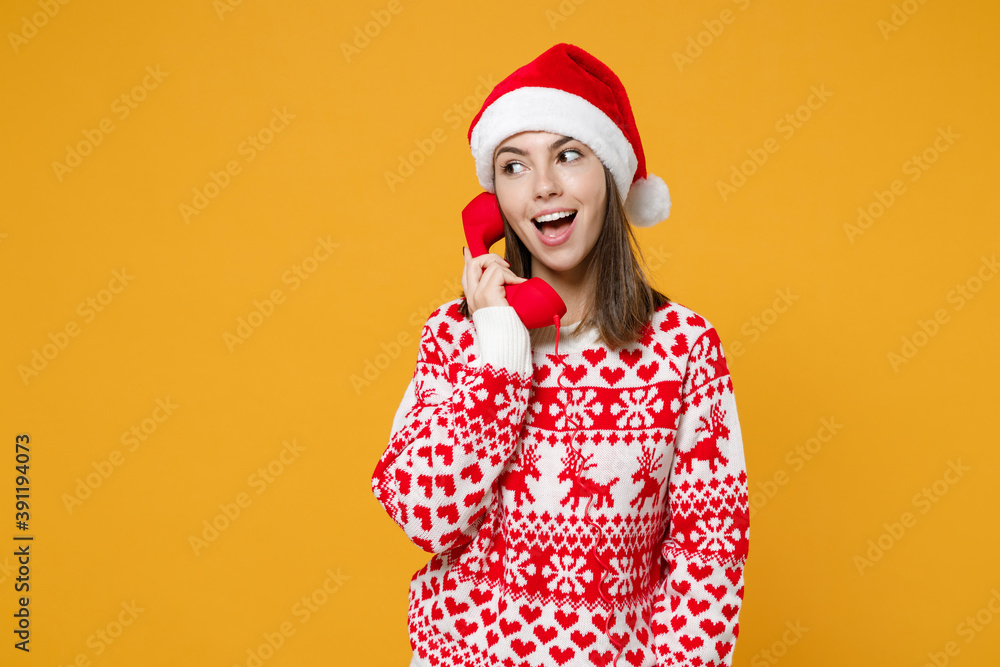 Excited young brunette Santa woman 20s wearing red sweater Christmas hat talking on telephone isolated on yellow colour background, studio portrait. Happy New Year celebration merry holiday concept. Excited young brunette Santa woman 20s wearing red sweater Christmas hat talking on telephone isolated on yellow colour background, studio portrait. Happy New Year celebration merry holiday concept.