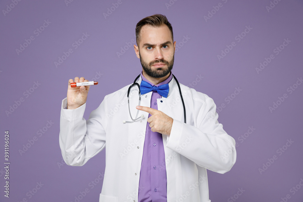 Serious young bearded doctor man in white medical gown stethoscope pointing index finger on blood test result sample tube isolated on violet background. Healthcare personnel health medicine concept.