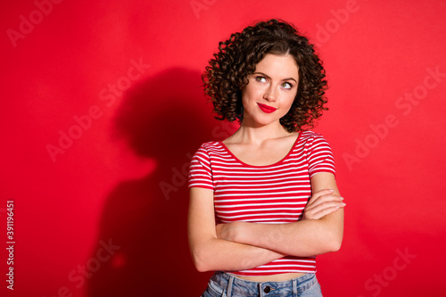 Photo of shiny pretty curly young lady wear casual striped outfit arms crossed looking empty space isolated red color background