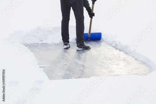 Young adult man cleaning white fresh snow with shovel from ice surface for ice skating. Winter routine concept. Back view. © fotoduets