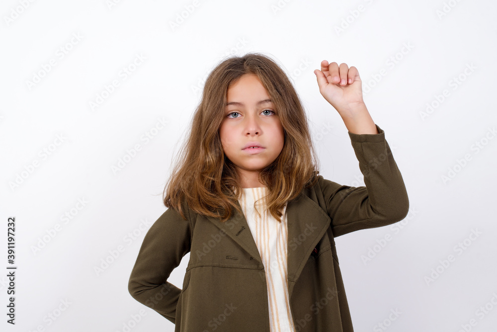 Beautiful little girl standing against white background, feeling serious, strong and rebellious, raising fist up, protesting or fighting for revolution. Beautiful little girl standing against white background, feeling serious, strong and rebellious, raising fist up, protesting or fighting for revolution.