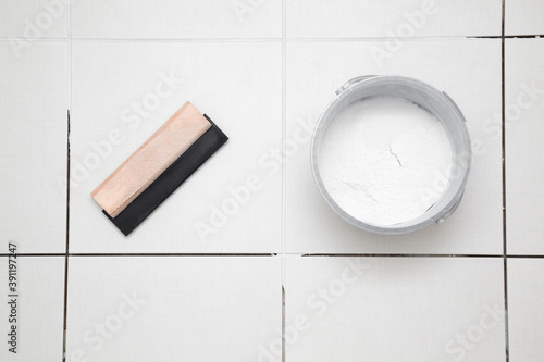 Rubber trowel and container with powder of grouting paste for ceramic tile seams on floor. Closeup. Top down view. photo