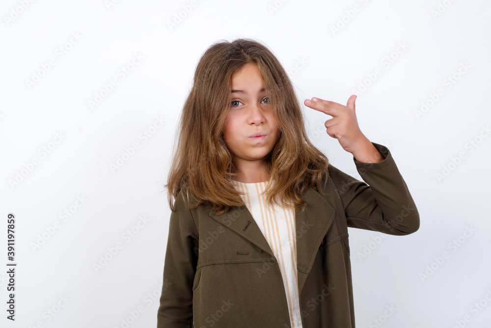 Unhappy Beautiful little girl standing against white background, imitates gun shoot makes suicide gesture keeps two fingers on temples. Unhappy Beautiful little girl standing against white background, imitates gun shoot makes suicide gesture keeps two fingers on temples.