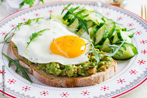 Healthy breakfast. Christmas brunch. Avocado sandwich with fried egg and fresh salad cucumber with arugula for healthy breakfast or snack.