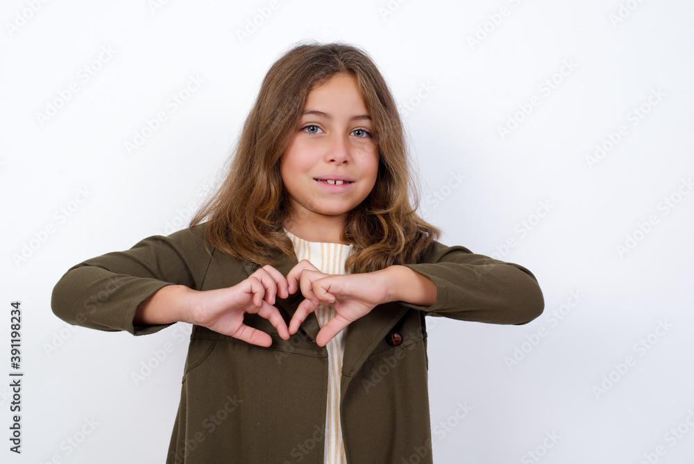 Beautiful little girl standing against white background, smiling in love showing heart symbol and shape with hands. Romantic concept. Beautiful little girl standing against white background, smiling in love showing heart symbol and shape with hands. Romantic concept.