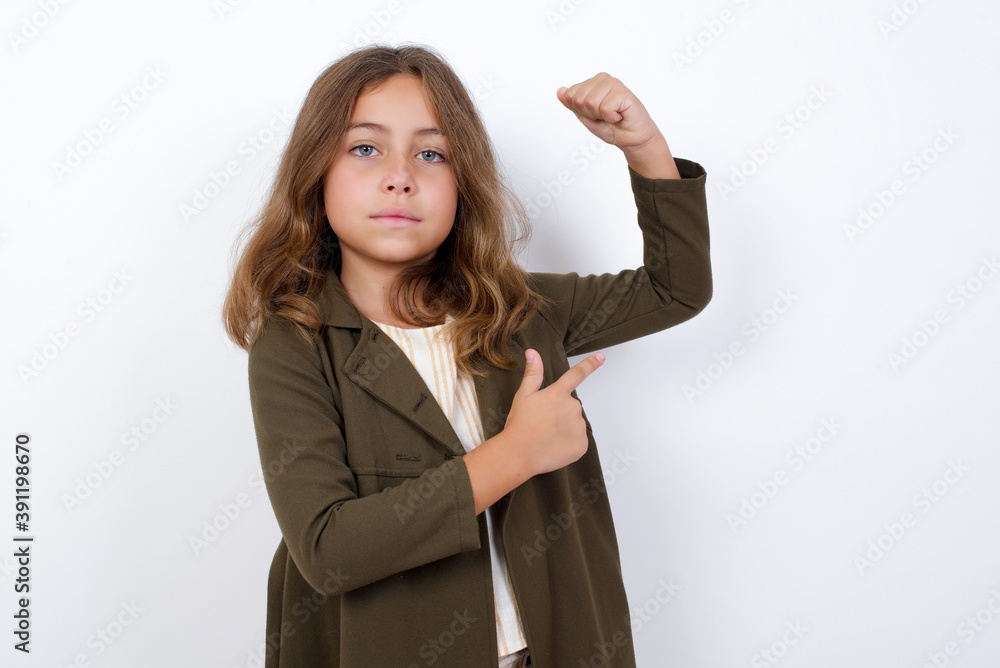 Smiling Beautiful little girl standing against white background, raises hand to show muscles, feels confident in victory, strong and independent. Smiling Beautiful little girl standing against white background, raises hand to show muscles, feels confident in victory, strong and independent.