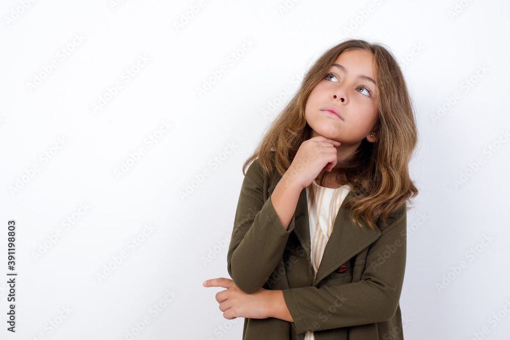 Face expressions and emotions. Thoughtful Beautiful little girl standing against white background, holding hand under his head, having doubtful look. Face expressions and emotions. Thoughtful Beautiful little girl standing against white background, holding hand under his head, having doubtful look.