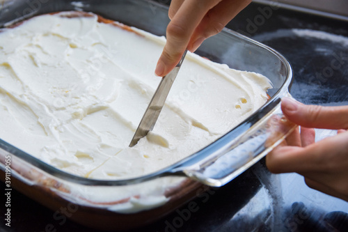 Woman hand cutting with a knife a baked cheese cake with whipped cream topping 
