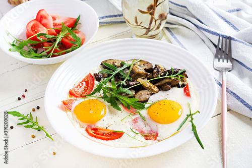 Tasty breakfast - fried eggs, forest mushrooms, tomatoes and arugula. Lunch food.