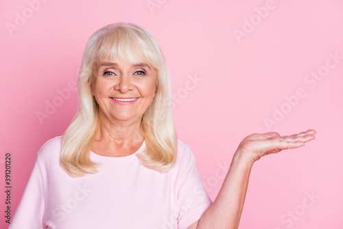 Photo portrait of cheerful grandmother keeping copyspace on hand smiling isolated on pastel pink color background