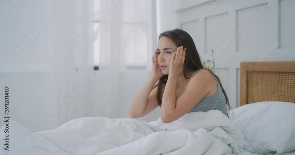 Woman Waking Up With Headache In Bed. Sleepy and tired young girl sitting on a bed struggling with headache Woman Waking Up With Headache In Bed. Sleepy and tired young girl sitting on a bed struggling with headache