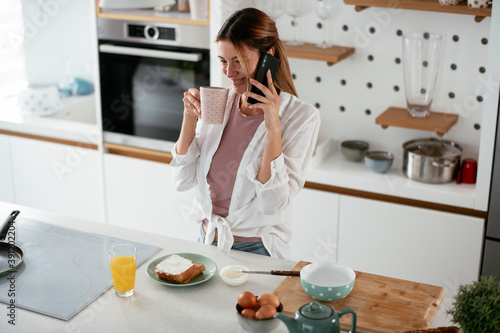 Young woman in kitchen. Beautiful woman preparing breakfast and using the phone..