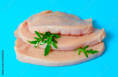 fresh turkey steaks with pepper and arugula on blue background