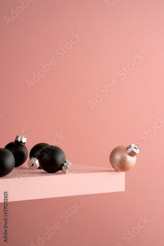 Several black and one pink Christmas ball on the pink shelf at the edge of the cliff. Pink background. Before the jump.