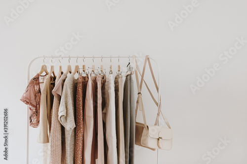 Women's minimal fashion pastel clothes. Stylish female blouses, sweaters, pants, jeans, t-shirts, handbags on hanger on white background. Fashion blog, website, social media hero header.