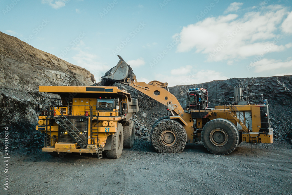 Obraz premium The wheel loader loads the ore into the mining dump truck. 