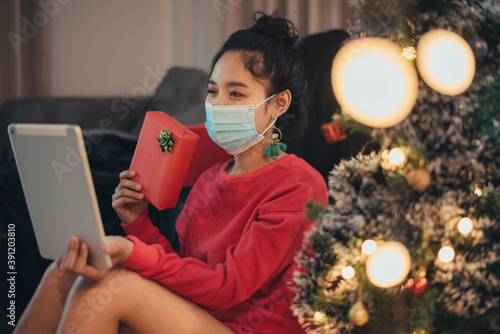 Woman weaing protective face mask and making video call on Christmas day. Christmas at home concept, New normal celebrating concept. photo