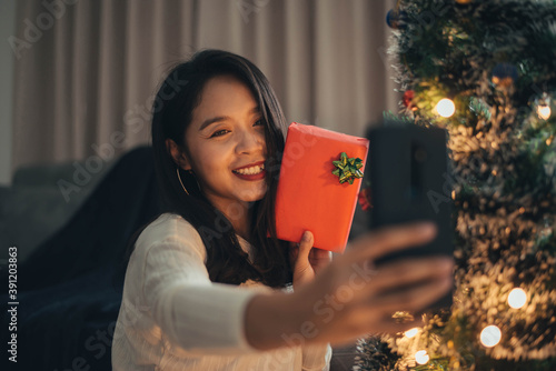 Woman making videocall her friends from home on Christmas day. Young smiling woman celebrating christmas with family and friends from smrtphone. photo