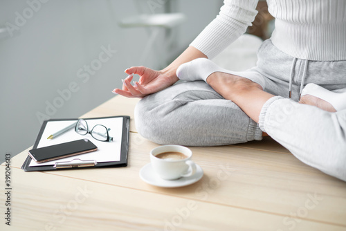 Closeup of a seated young woman's hand in a lotus position at the desktop with a cup of coffee.