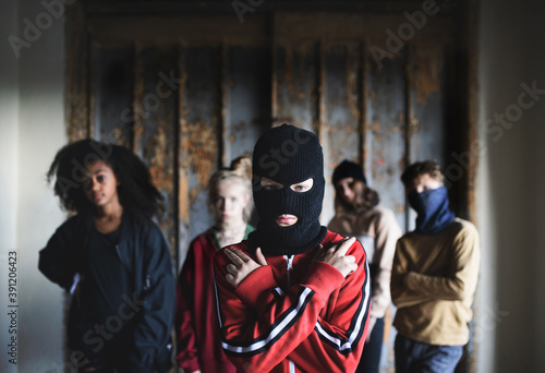 Boy with mask with teenagers gang indoors in abandoned building, showing finger gun gesture.