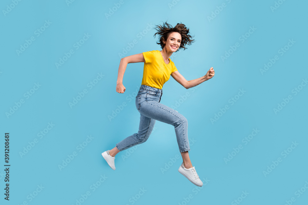 Obraz premium Full length profile photo of girl jump rush run fists wear yellow t-shirt denim jeans footwear isolated blue color background