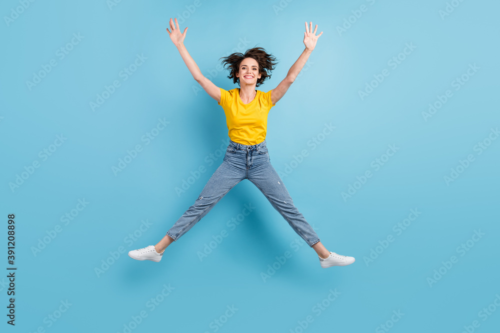 Full length photo of crazy girl jump star form raise hands wear yellow t-shirt jeans footwear isolated blue color background