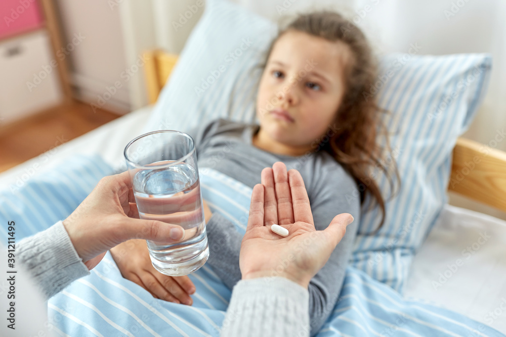 family, health and people concept - mother giving medicine to little sick daughter lying in bed at home family, health and people concept - mother giving medicine to little sick daughter lying in bed at home