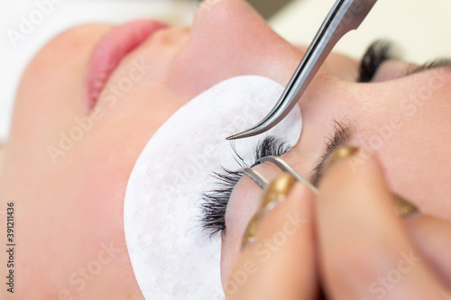 Eyelash extension procedure. Woman eye with long eyelashes. Close up. using tweezers