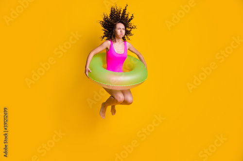 Photo portrait of young curly girl jumping into pool holding breath closed eyes with inflatable green circle wearing fuchsia swim wear isolated on vivid yellow colored background photo