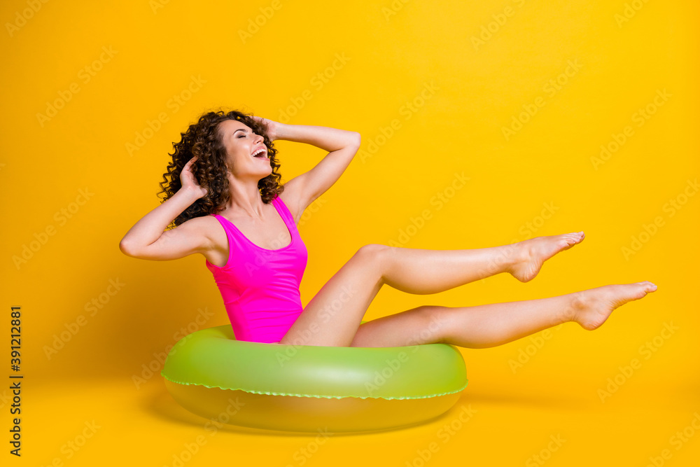 Photo portrait of funny brunette girl sitting in green inflatable ring touching hair wearing fuchsia swim wear isolated on bright yellow colored background Photo portrait of funny brunette girl sitting in green inflatable ring touching hair wearing fuchsia swim wear isolated on bright yellow colored background