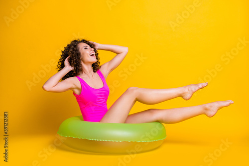 Photo portrait of funny brunette girl sitting in green inflatable ring touching hair wearing fuchsia swim wear isolated on bright yellow colored background
